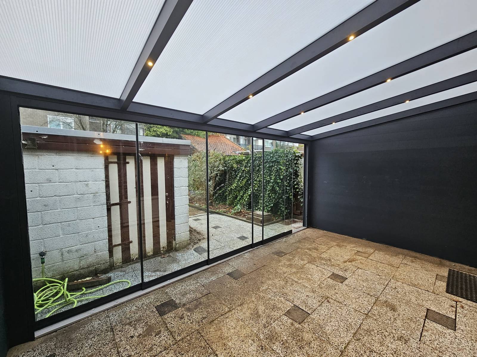 Houten veranda met glazen schuifdeuren, loungebank en uitzicht op de tuin
