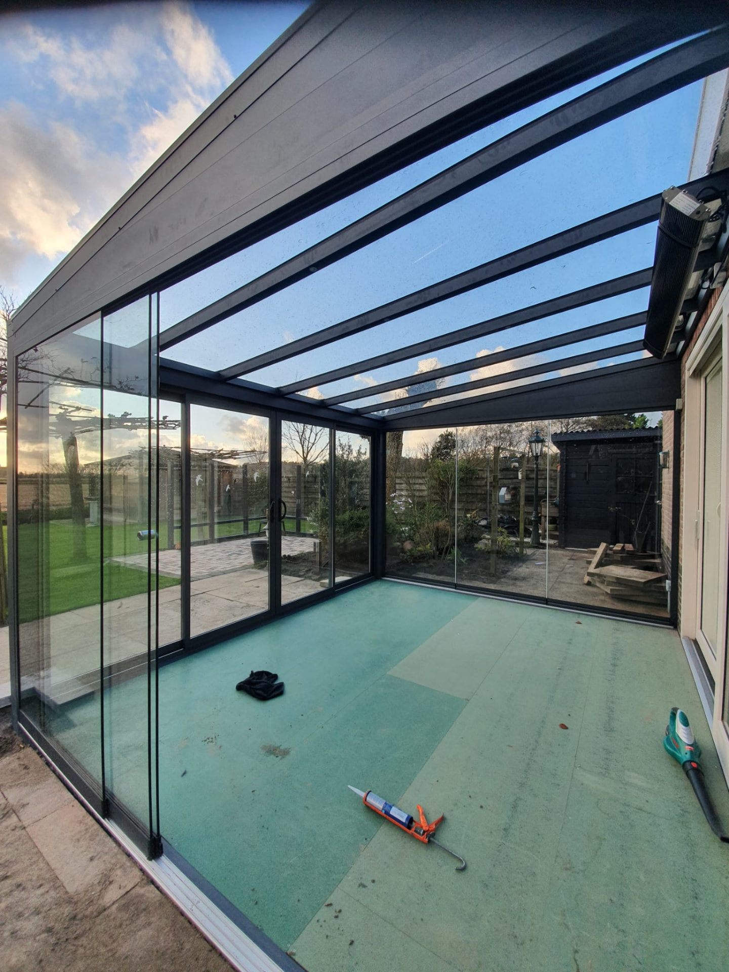 Aluminium overkapping met glazen dak en glazen schuifwanden aan een woning