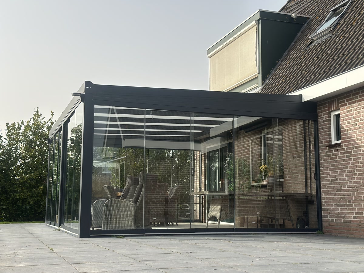 Moderne aluminium tuinkamer met glazen schuifwanden aangebouwd aan een bakstenen woning